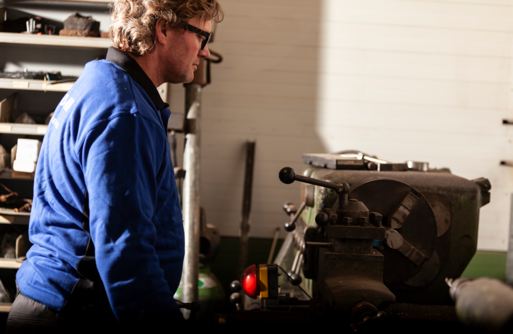 Vakman in blauwe werkkleding bedient metaalbewerkingsmachine in professionele werkplaats