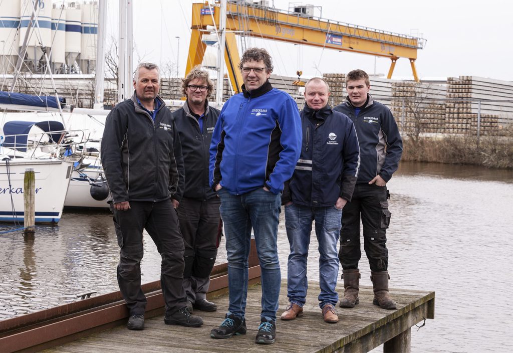 Professioneel scheepsonderhoud team van Zuiderbaan Totaal Service poseren op steiger in haven met werkboot